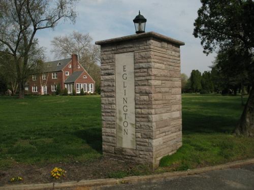 Stone sign reading "Eglinton" in front of a large brick house, surrounded by green grass and trees.