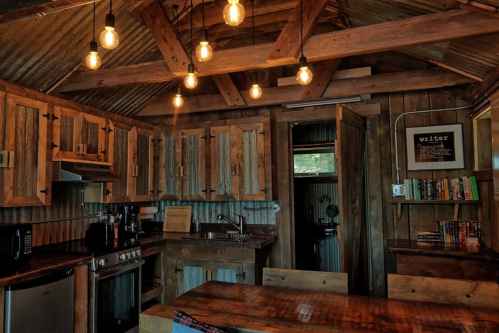 Cozy rustic kitchen with wooden cabinets, a dining table, and warm pendant lights hanging from a metal roof.
