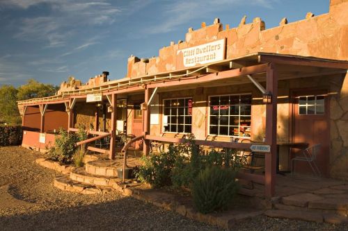 Exterior of Cliff Dwellers Restaurant, featuring stone architecture and a welcoming porch in a desert setting.