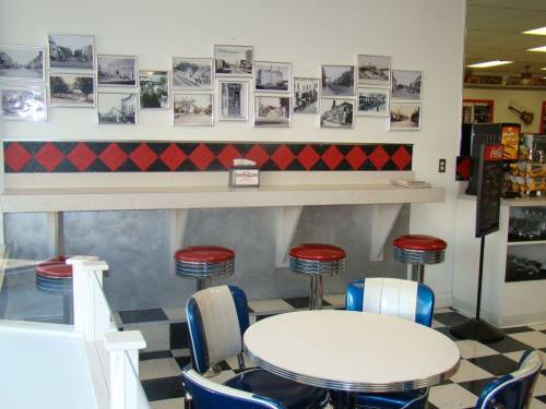 A retro diner interior featuring a round table, red and silver stools, and black and white checkered flooring.
