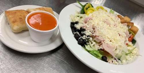 A plate with a fresh salad topped with cheese, alongside a cup of tomato soup and a piece of bread.