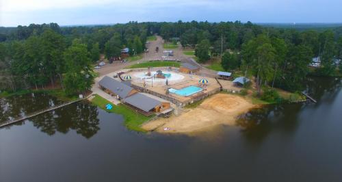 Aerial view of a lakeside camp with a pool, cabins, and recreational areas surrounded by trees.