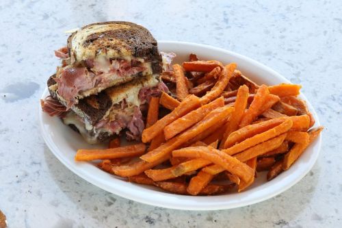 A plate with a stacked sandwich filled with meat and cheese, accompanied by a side of crispy sweet potato fries.