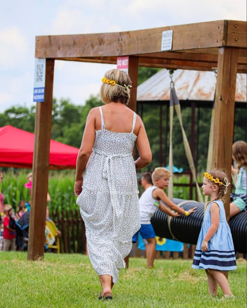A woman in a polka dot dress walks towards a playground, while children play nearby under a sunny sky.