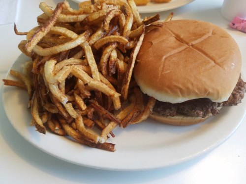 A plate with a hamburger in a bun next to a generous serving of crispy, golden-brown French fries.