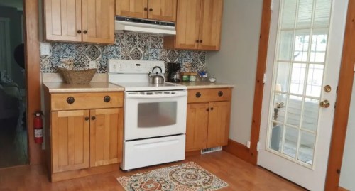 A cozy kitchen with wooden cabinets, a white stove, and a decorative rug, featuring a glass door leading outside.