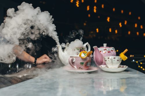 A whimsical tea setup with steaming teapots, cups, and smoke, set against a softly lit background.