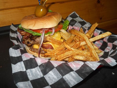 A juicy burger with bacon, cheese, lettuce, tomato, and onion, served with crispy fries in a checkered basket.