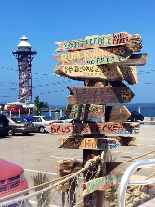 Colorful directional signs at a waterfront, pointing to various attractions like the North Pole and local eateries.