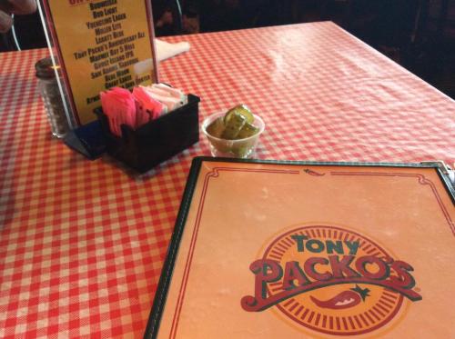 A checkered tablecloth with a menu for Tony Packo's and a small dish of pickles on the side.