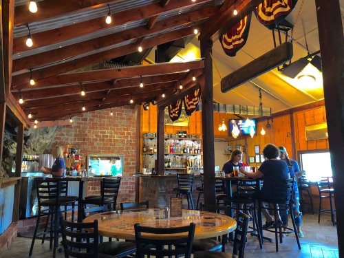 Cozy restaurant interior with wooden beams, string lights, and patrons enjoying drinks at tables and the bar.