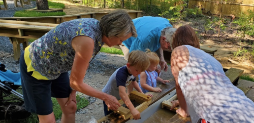A group of adults and children work together on a woodworking project outdoors, focused and engaged.