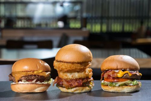 Three delicious burgers on a table: a cheeseburger, a crispy onion ring burger, and a bacon cheeseburger.