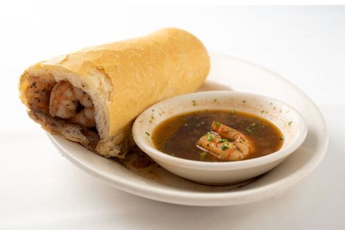 A shrimp po' boy sandwich served with a side of shrimp broth in a small bowl.