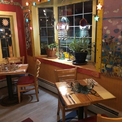 Cozy restaurant interior with colorful decor, potted plants, and wooden tables set for dining. Warm, inviting atmosphere.