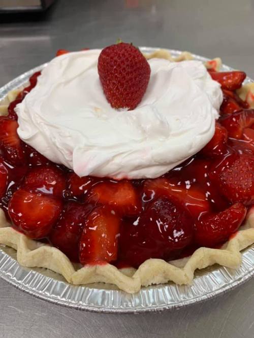 A delicious strawberry pie topped with whipped cream and a fresh strawberry, set in a flaky crust.