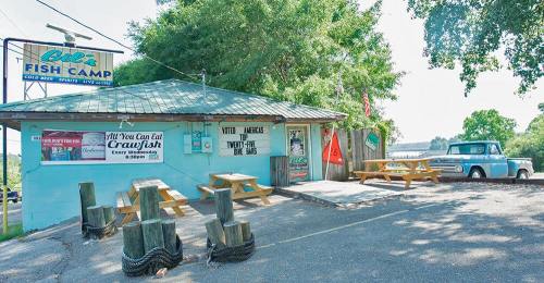 A small fish camp with picnic tables outside, a vintage truck parked nearby, and a sign advertising crawfish.