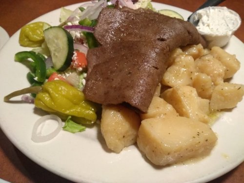 A plate featuring sliced meat, boiled potatoes, and a fresh salad with cucumbers, tomatoes, and a side of dressing.