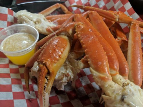 A plate of crab legs with a small cup of melted butter, served on red and white checkered paper.