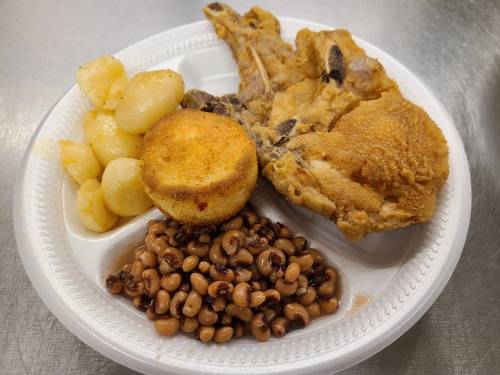 A plate with fried chicken, cornbread muffin, black-eyed peas, and seasoned potatoes.