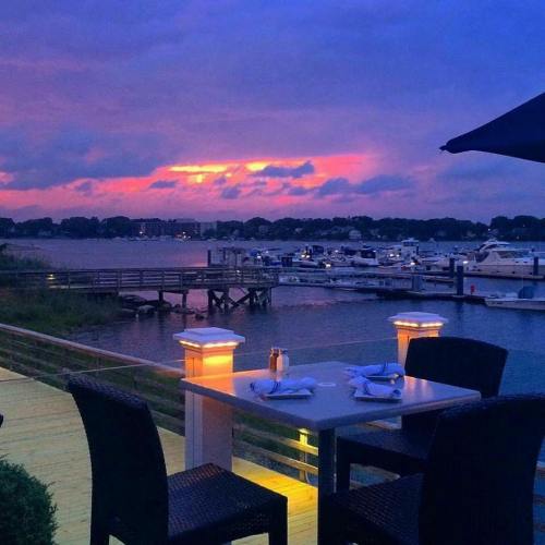 A serene waterfront view at sunset, featuring a table set for dining and boats docked in the background.