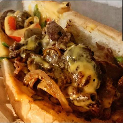 A close-up of a loaded sandwich with grilled steak, sautéed onions, peppers, and melted cheese in a toasted bun.