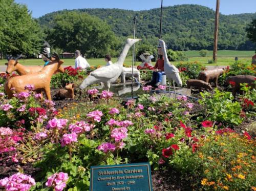 Colorful garden scene featuring animal sculptures among vibrant flowers, with a sign for Schlosstein Gardens in the foreground.