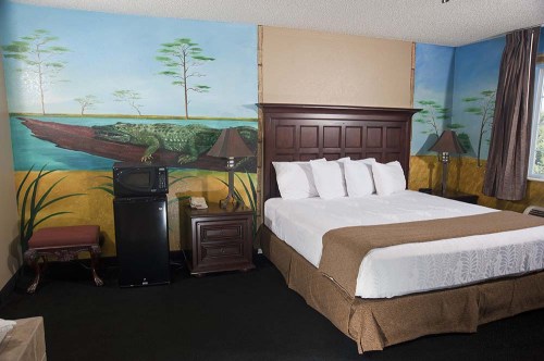A hotel room featuring a bed, nightstands, a mini fridge, and a mural of a crocodile on the wall.
