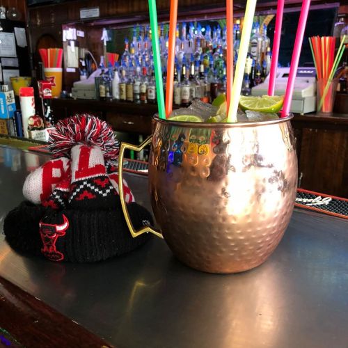A copper mug filled with drinks and colorful straws, next to a black and red knit hat on a bar counter.