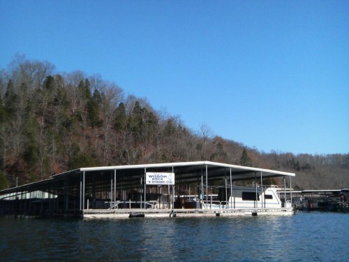 A boat dock on a calm lake, surrounded by trees and a clear blue sky.