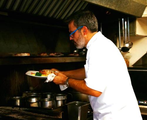 A chef in a kitchen carefully plating a dish with vegetables, focused on his work in a busy cooking environment.