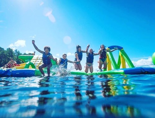 A group of children joyfully jumping into a lake from a colorful inflatable water slide on a sunny day.