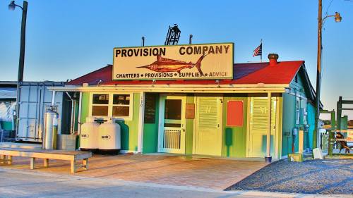 Colorful building with a sign reading "Provision Company," featuring fishing charters and supplies, under a clear blue sky.