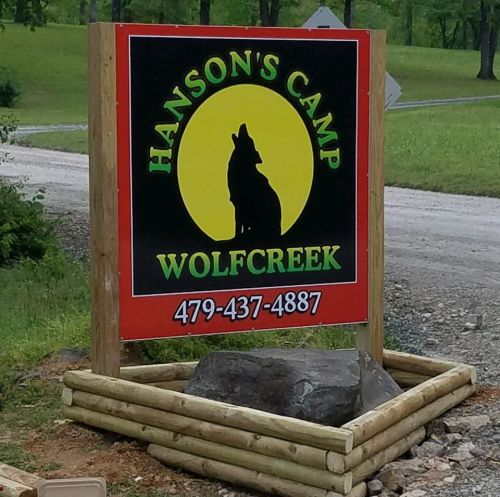 Sign for Hanson's Camp Wolfcreek featuring a silhouette of a wolf against a yellow circle, with contact information below.
