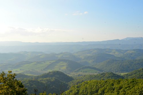 A panoramic view of rolling green hills and mountains under a clear blue sky.