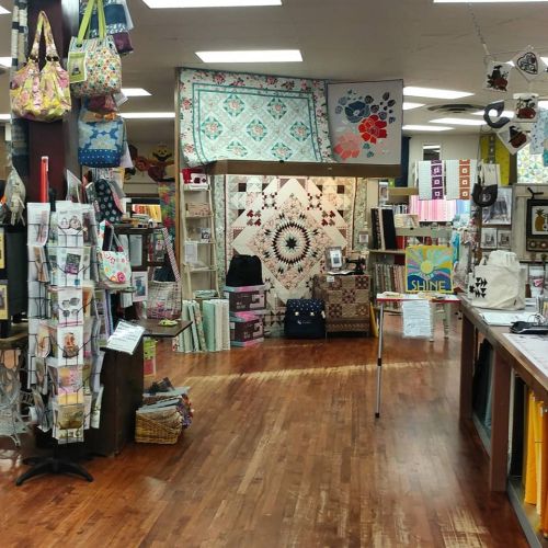 A cozy craft store interior featuring colorful quilts, fabric, and various sewing supplies on display.