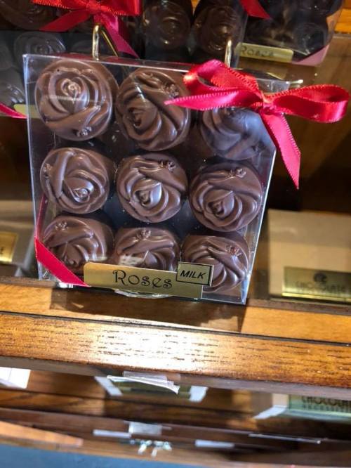 A box of chocolate rose-shaped candies tied with a red ribbon, labeled "Roses Milk."