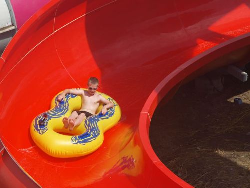 A child slides down a red water slide on a yellow inflatable tube, enjoying a sunny day at a water park.