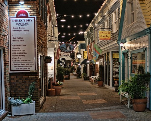 A charming, illuminated alleyway lined with shops and decorative lights, creating a cozy evening atmosphere.