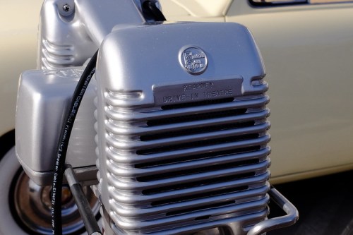 Close-up of a vintage drive-in theater speaker, silver with "Kearney Drive-In Theatre" engraved on it.
