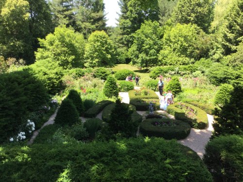 A lush garden with neatly trimmed hedges, colorful flowers, and visitors exploring the serene landscape.