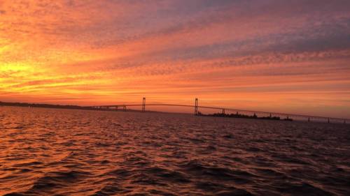A vibrant sunset over water, with a bridge silhouetted against the colorful sky.