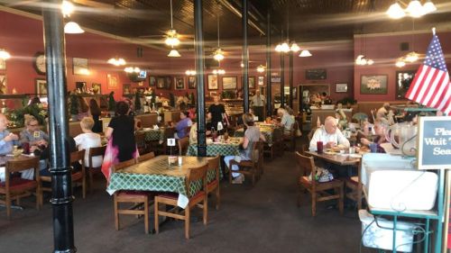 A bustling restaurant interior with diners at tables, colorful decor, and an American flag in the corner.
