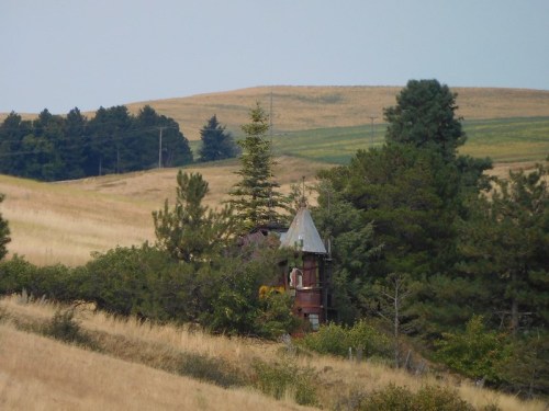 A rustic tower surrounded by trees and rolling hills under a clear sky.