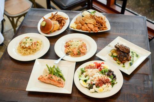 A table with various dishes: pasta, seafood, salad, salmon, a burger, fries, and chicken, all beautifully presented.