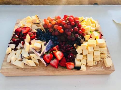 A wooden platter filled with assorted cheeses, fresh strawberries, blueberries, grapes, and dried fruits.
