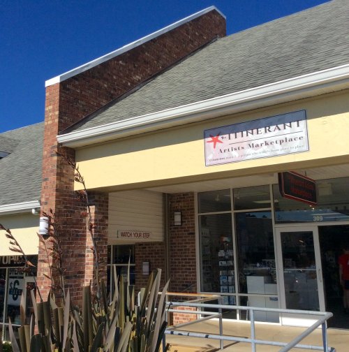 Exterior of a brick building featuring a sign for "Itinerant Artists Marketplace" and a warning to "Watch Your Step."
