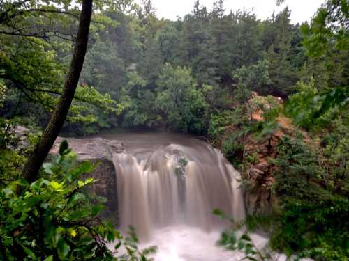 A serene waterfall cascades over rocks, surrounded by lush green trees and foliage.