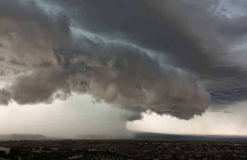 Dramatic storm clouds loom over a vast landscape, with rain falling in the distance against a moody sky.