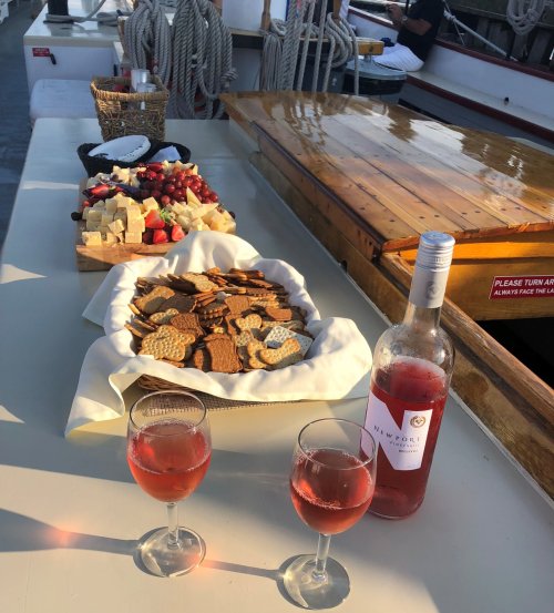 A table on a boat with snacks, cheese, fruit, and two glasses of rosé wine.